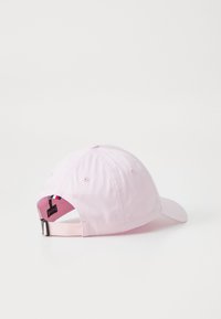 Rosa stoffcaps med buet skygge, justerbar reim bak, og en fargerik etikett med røde, hvite og blå striper inni.