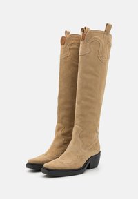 Botas de vaquero de ante marrón con costuras decorativas, de altura media hasta la pantorrilla, punta afilada y un tacón grueso negro. Incluyen tiradores en la parte superior.