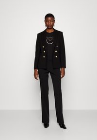 Blazer nero su misura con doppio bottone dorato, top con perline nere e pantaloni abbinati. Presenta una vestibilità slim e una texture morbida.