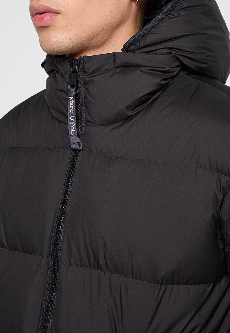 Schwarze gepolsterte Jacke mit Reißverschluss, hohem Kragen und weicher Textur. Mit Marc O'Polo-Branding am Reißverschluss-Zipper.