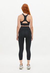 Svart sportbh med hakut i ryggen, kombinerad med högmidjade svarta leggings. Outfitten har en slät textur och en figurnära design.