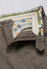 Pantaloni khaki con una superficie texturizzata, caratterizzati da una fodera interna stampata in blu e giallo, chiusura a pulsante e una tasca laterale con zip.