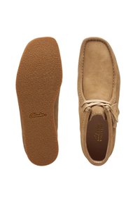 Mocasines de ante color marrón, con suela de goma con textura antideslizante, puntera redonda y un acento de cordones en la parte superior.