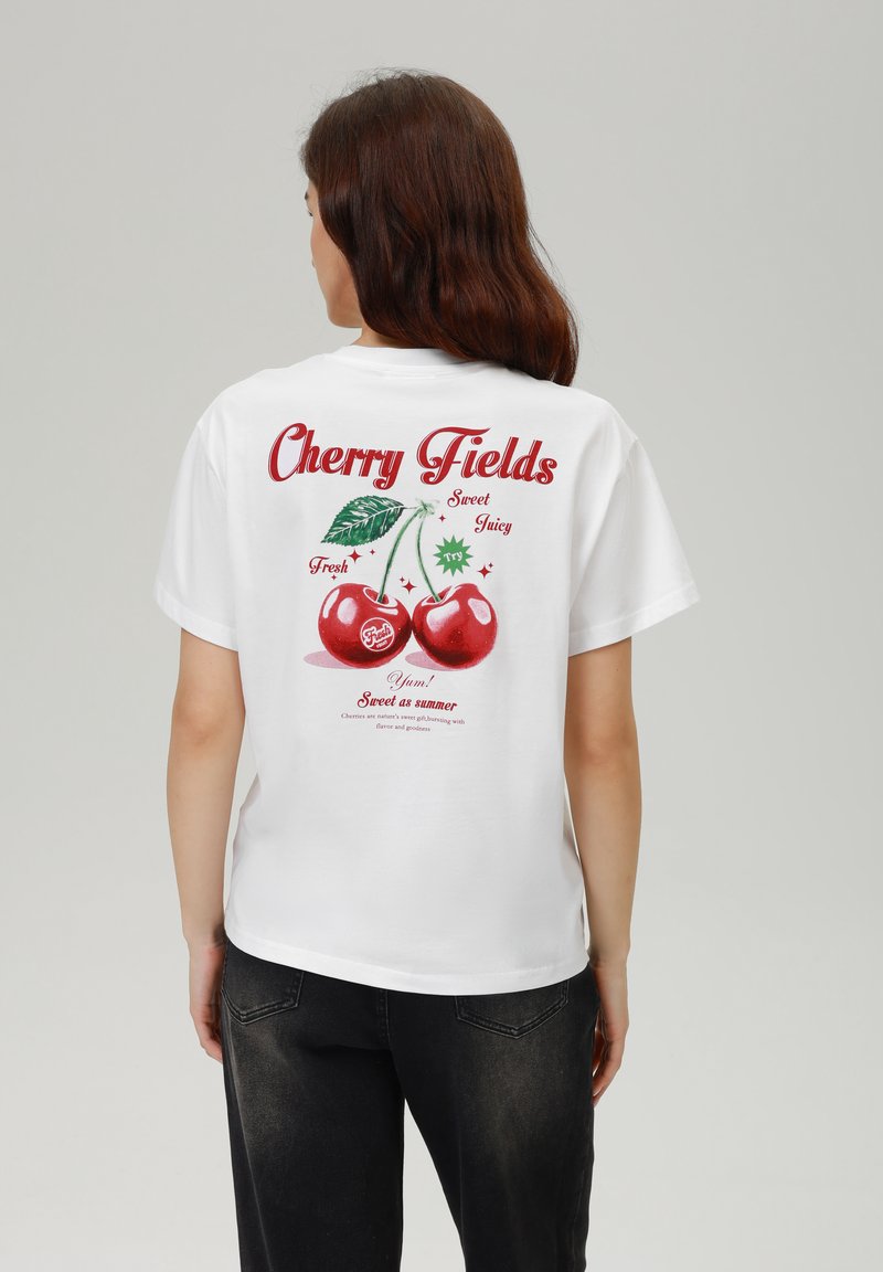 Balts kokvilnas T-krekls ar sarkanu ķiršu grafiku uz muguras, kurā ir teksts "Cherry Fields" un informācija par ķiršiem. Īsas piedurknes, brīva piegriezne.