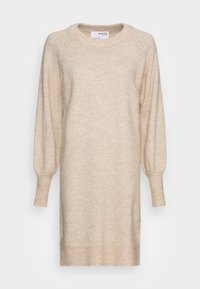 Abito lavorato a maglia beige con scollatura rotonda, maniche lunghe a palloncino e polsini a coste. Il tessuto ha una consistenza morbida e pelosa e una vestibilità rilassata.