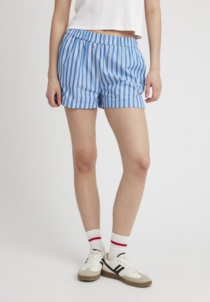 Shorts rayés bleus avec une taille élastique, présentant des rayures verticales blanches et une coupe décontractée, associés à des baskets blanches et des chaussettes.
