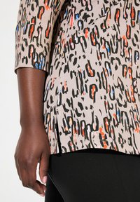 Korte mouw top in beige stof met een abstract meerkleurig patroon, met zwarte, rode en blauwe accenten; zijsplitten aan de onderrand.