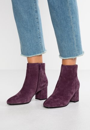 Lilla ruskindsstøvler til anklerne med en blokhæl, der har en lynlås i siden og en spids tå, parret med cropped denimbukser med frynset kant.