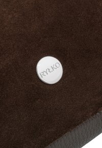 Superficie de ante y cuero marrón con una pequeña placa metálica redonda grabada con "RYŁKO" en el centro.
