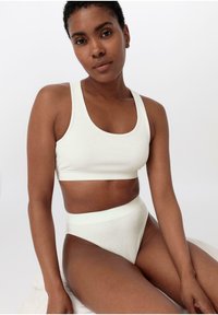 Ljus gräddfärgad ribbad crop top och högmidjade trosor set. Slät textur, åtsittande design och minimala sömmar för komfort.