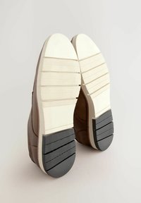 Zapatos marrones con una superficie texturizada; las suelas de plataforma blanca presentan ranuras horizontales y una banda de rodadura de goma oscura en el talón para mayor agarre.