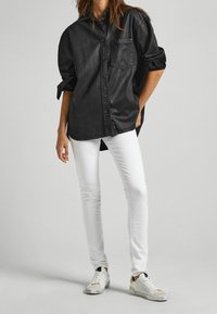 Svart denimskjorta med knapp-up och bröstficka, tillsammans med figurnära vita jeans och vita sneakers med beige detaljer.