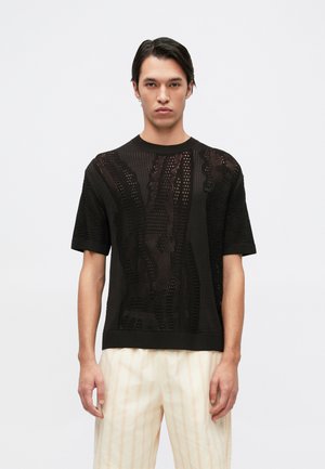Maglione nero a maniche corte lavorato a maglia con un motivo testurizzato. Il tessuto presenta intrecci aperti, creando un aspetto leggero.