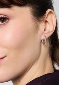 Srebrna obrączka na kolczyku, prezentowana na uchu modelki, charakteryzująca się eleganckim, nowoczesnym wzornictwem z polerowanym wykończeniem i gładką powierzchnią.