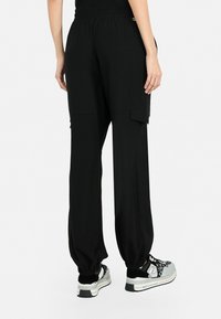 Pantalons cargo noirs avec une taille élastique, des poches latérales, une coupe décontractée et des ourlets fuselés, associés à des baskets noires et grises.