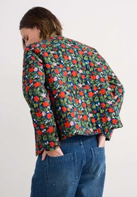 Veste matelassée avec un motif floral en rouge, rose et vert sur fond bleu foncé ; présente une coupe courte et une coupe décontractée.