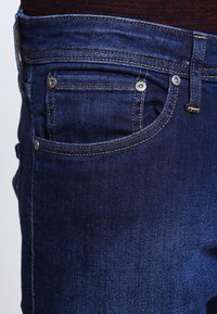 Mörkblå denimjeans med en klassisk femficksdesign, synlig sömnad och metalldetaljer på fickorna.