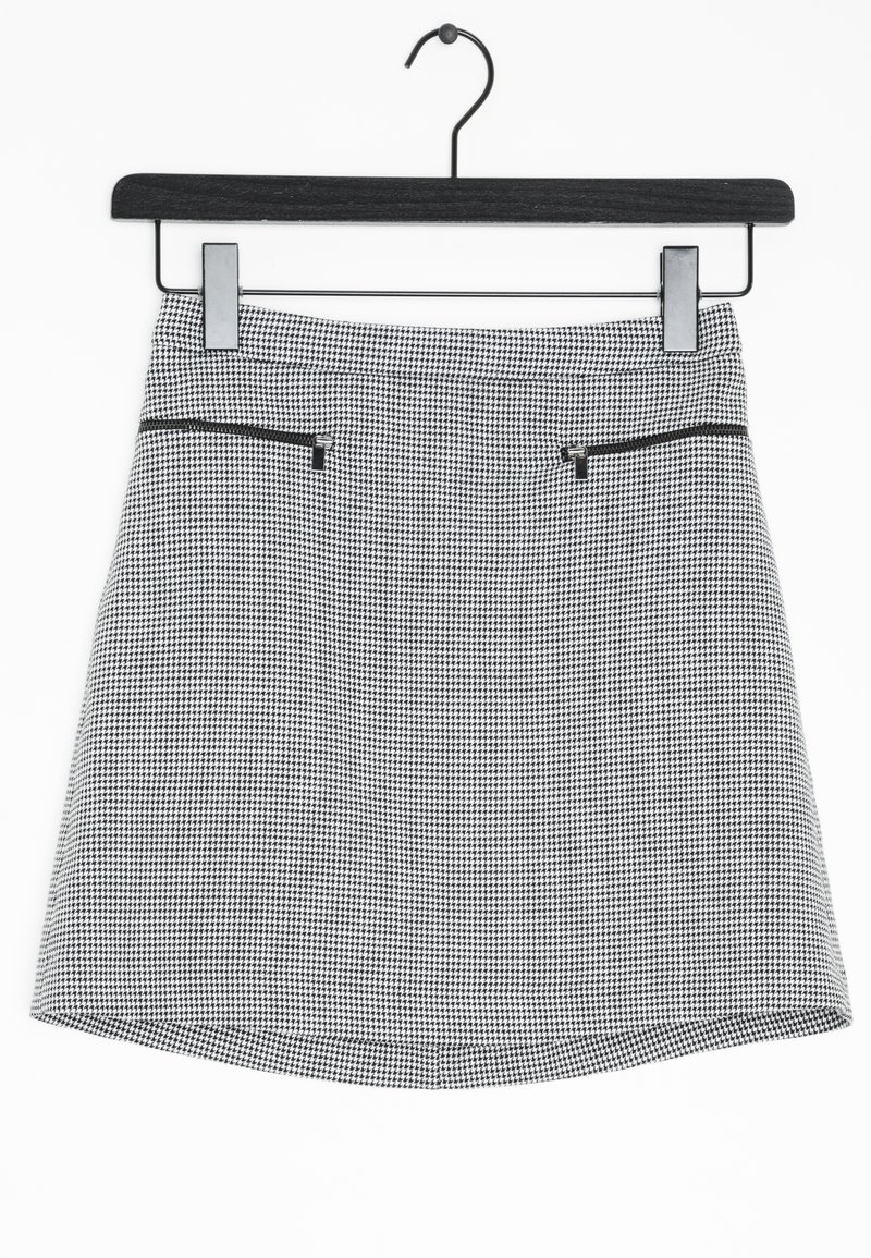 Mini-jupe pied-de-poule noire et blanche avec deux poches zippées horizontales, suspendue sur un cintre noir sur fond blanc.