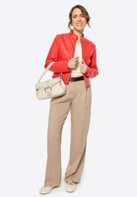 Veste en cuir rouge, top crème, pantalon beige à larges jambes et chaussures blanches. Sac à bandoulière avec détails cloutés et boucle. Design simple et moderne.