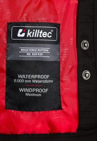 Étiquette en tissu noir arborant le logo "killtec", avec un fond rouge. Indique "IMPERMÉABLE" (8 000 mm) et "COUPE-VENT", avec des détails cousus.