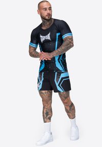 Melns sporta krekls ar ziliem akcentiem un logotipu, apvienots ar melniem šortiem ar ziliem ģeometriskiem rakstiem. Gluda, elastīga materiāls.