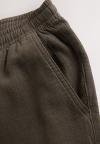 Dark gray jogger pants with an elastic waistband, textured fabric, and side pockets; features visible stitching and a relaxed fit.