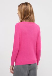 Fitted rosa Strickpullover mit langen Ärmeln und Rundhalsausschnitt, der eine glatte Textur aufweist. Getragen mit grauen, gestreiften Hosen, von hinten aufgenommen.