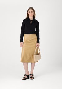 Svart langermet bluse med nøkkelhullsdetalj, beigefarget skinn midi-skjørt, svarte sandaler med gullakenter, og en beige håndveske.