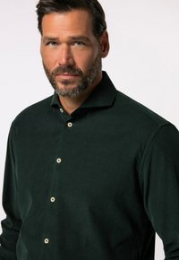 Camicia in velluto a coste verde scuro con design a bottoni, caratterizzata da un colletto strutturato e una sottile trama rigata, accentuata da bottoni di colore chiaro.