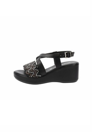 Sandalo con zeppa nera caratterizzato da una tomaia intrecciata testurizzata con accessori metallici. Cinghia regolabile alla caviglia e una soletta liscia e confortevole.