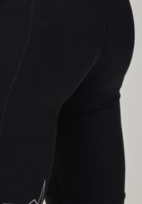 Schwarze Sportshorts aus dehnbarem Material, mit glatter Textur und flachen Nähten, versehen mit einem weißen geometrischen Muster an der Seite.