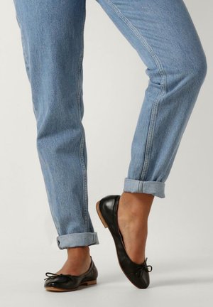 Zwarte leren ballerina's met een ronde neus, kleine strikaccent en lage houten hak, gedragen met opgerolde lichtblauwe denim jeans.