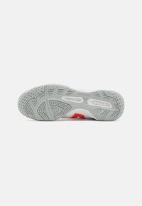 Suela de una zapatilla deportiva que presenta un material de goma gris con un patrón texturizado, acentuada por secciones rojas y detalles que no marcan.