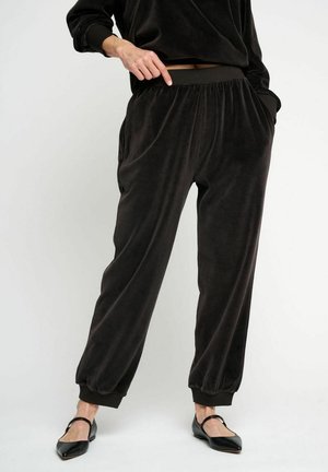 Pantaloni jogger neri in peluche con vita e polsini elasticizzati, dotati di tasche laterali e una superficie morbida. Abbinati a ballerine nere.