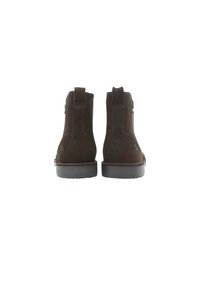 Botas de ante marrón hasta el tobillo con punta redondeada, tiradores de tela verticales y una suela de goma plana. Detalles de costura sutiles en los lados.