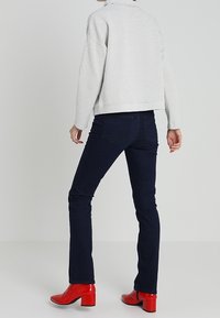 Veste grise texturée avec un col montant, associée à un jean bootcut bleu foncé et des bottines rouges à talons brillantes.