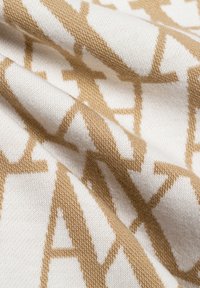 Gebreid textiel met een crèmekleurige achtergrond en een herhaald bruin patroon van letters, dat een zachte textuur en een gladde afwerking laat zien.