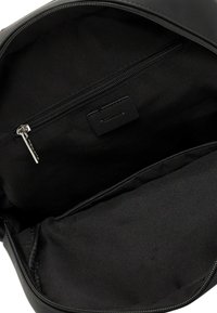 Zwarte backpack binnenkant met een zakje met ritssluiting, stoffen voering en een klein rechthoekig merklabel onder de rits.