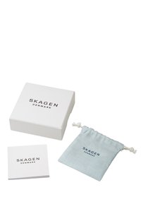 Biały pudełko z logo "SKAGEN DENMARK", jasnoniebieski materiałowy woreczek i mała broszura. Pudełko ma gładkie wykończenie; woreczek jest teksturowany.