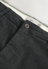 Dark gray trousers with a textured fabric, featuring a button closure and waistband label. Includes subtle stitching details along the edges.