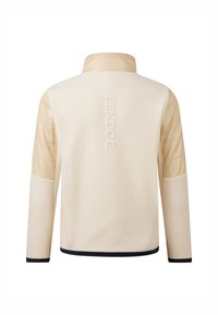 Beige fleecejakke med polstrede beige skuldre, marineblå kant ved ærmer og kanten, og præget logo på ryggen. Standard kravedesign.