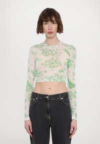 Langermet cropped topp laget av gjennomsiktig stoff med grønt blomsterprint; har rund hals og tettsittende silhuett. Kombinert med mørke jeans.