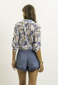 Blouse transparente à manches longues avec un motif floral bleu sur un fond à pois, associée à un short en denim taille haute avec des revers.