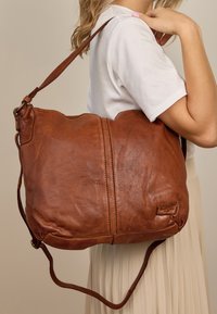 Braune Leder-Schultertasche mit strukturiertem Oberfläche, abgerundetem Top und verstellbarem Gurt. Verfügt über einen sichtbaren Reißverschluss und ein Logo-Detail.