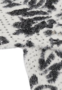 Indumento lavorato a maglia in bianco e nero, caratterizzato da una texture morbida e pelosa con un motivo floreale, arricchito da piccoli dettagli metallici.
