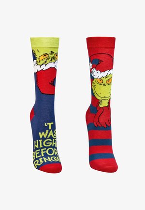 Bunte Socken mit einem Cartoon-Grinch-Design; eine Socke hat rote Streifen, die andere ist blau mit gelbem Text. Weiches Strickmaterial.
