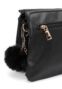 Bolso de mano de piel negra con una superficie texturizada, que cuenta con un bolsillo con cremallera y un pom pom de piel sintética negra decorativo, sujeto por una cadena dorada.