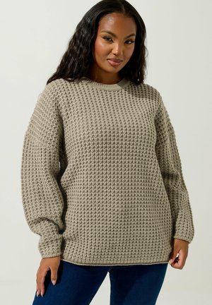 Chunky gestrickter beiger Pullover mit rundem Halsausschnitt und überschnittenen Schultern, der ein strukturiertes gewebtes Muster und gerippte Bündchen aufweist.