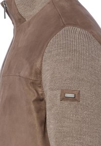 Brązowa kurtka dwutonowa z gładkiej skóry na korpusie i teksturowanymi dzianinowymi rękawami. Zamek błyskawiczny z przodu oraz naszywka z logo na rękawie.