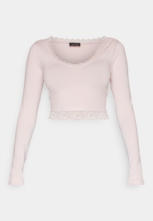 Haut court à manches longues en coton rose doux. Il présente une bordure en dentelle festonnée au niveau du col et de l'ourlet, offrant une texture délicate.